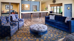 A hotel lobby with a reception desk, blue upholstered sofas, a patterned carpet, and a decorative wall.