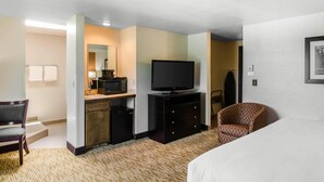 A hotel room with a bed, a desk with a TV, a chair, and a microwave.