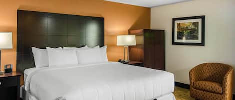 A hotel room with a large bed, a nightstand with a lamp, a chair, and a framed picture on the wall.