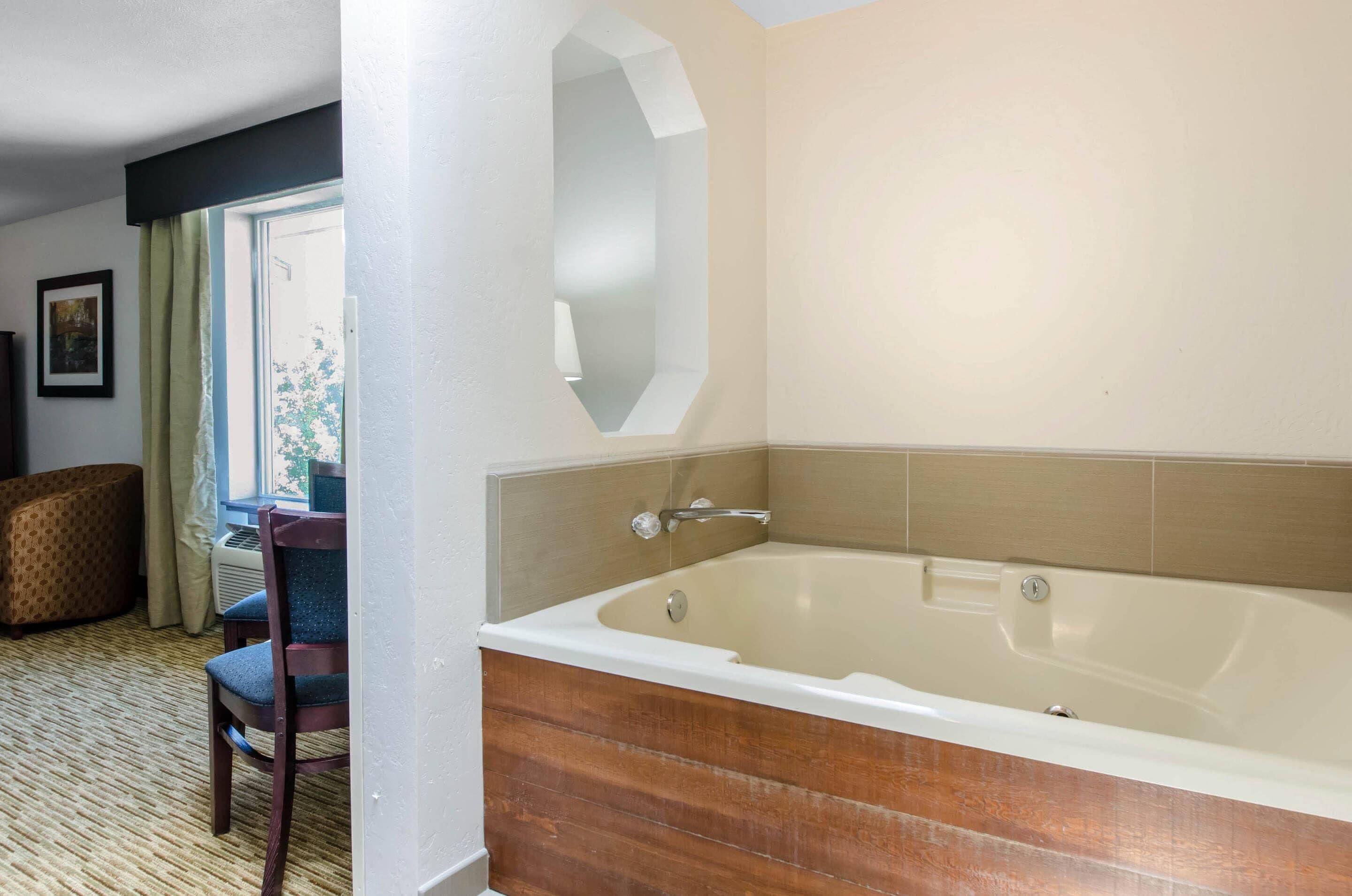 Un baño con una bañera grande, un tocador de madera y una silla cerca de una ventana.
