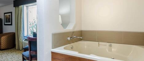 Un baño con una bañera grande, un tocador de madera y una silla cerca de una ventana.