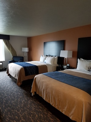 A hotel room with two beds, a desk, and a chair.