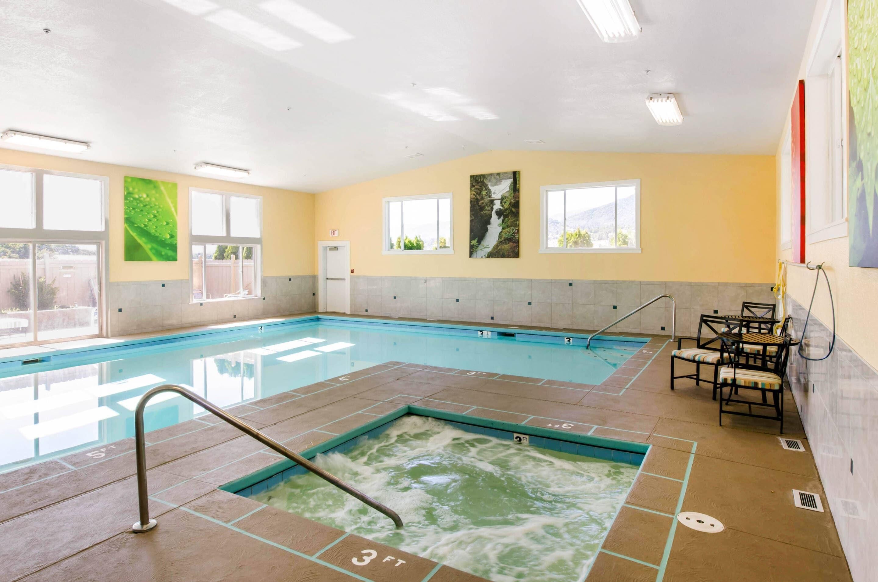An indoor swimming pool with clear water, tiled floor, and a hot tub area.