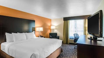 A hotel room with a large bed, a desk with a television, a chair, and a window with curtains.