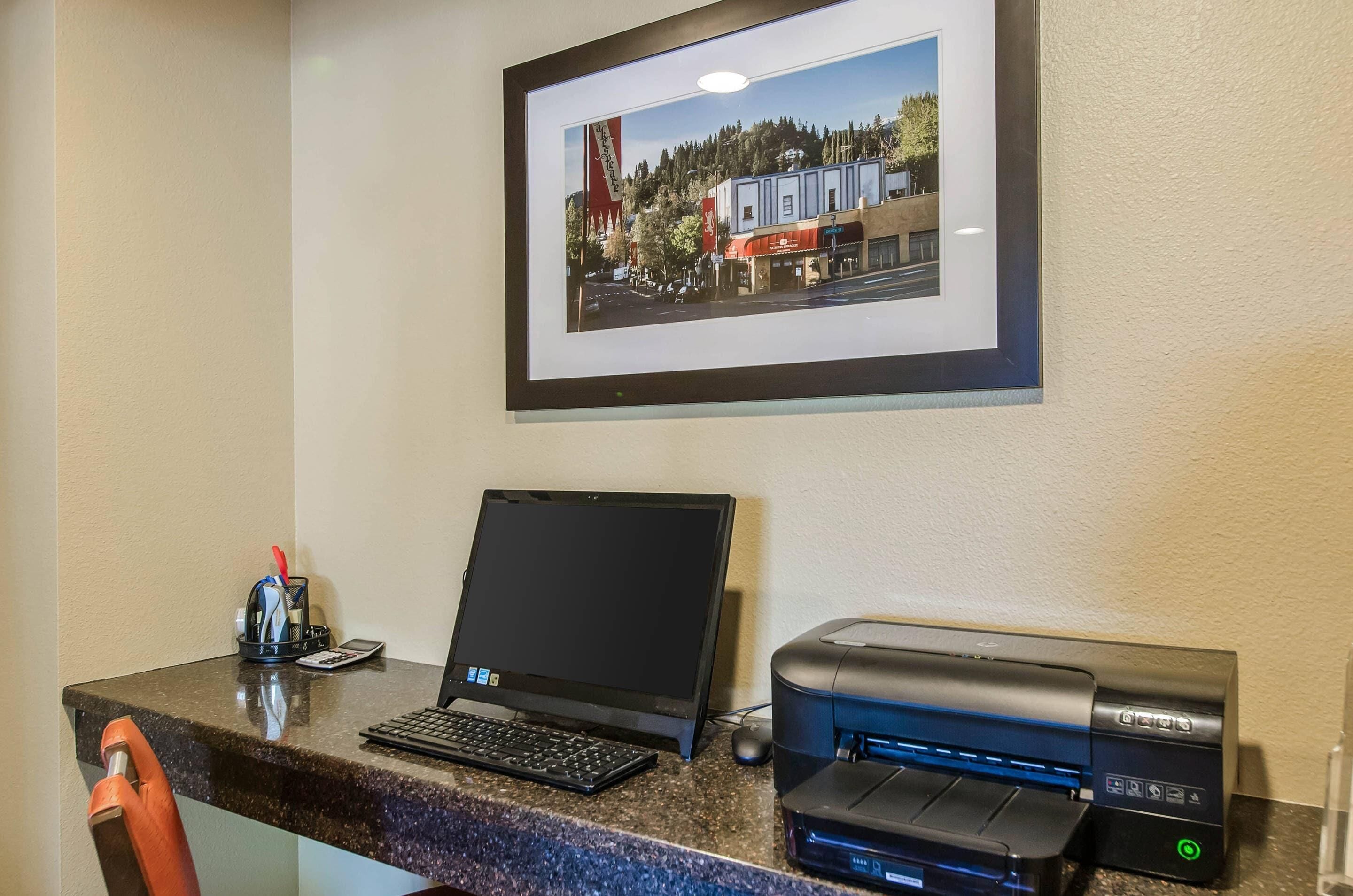 Een receptiebalie met een laptop, een printer en een ingelijst foto van een stad aan de muur.