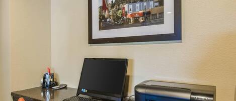Een receptiebalie met een laptop, een printer en een ingelijst foto van een stad aan de muur.