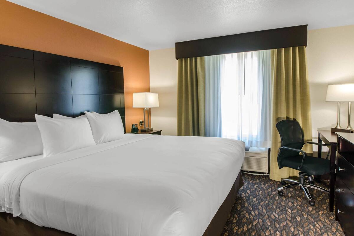 Una habitación de hotel con una cama grande, un escritorio con silla, una lámpara y una ventana con cortinas.