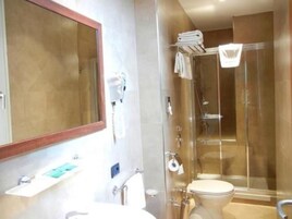 Et badeværelse med stort spejl, vask, toilet og brusekabine med glasvægge.