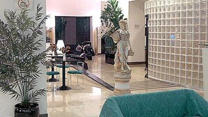 Un vestíbulo con mostrador de recepción, zona de estar, plantas en macetas y una estatua.