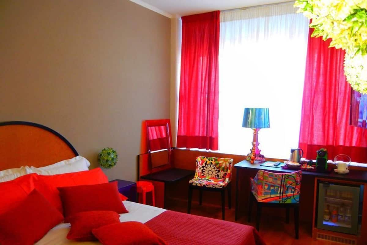 A hotel room with a bed, a desk, a chair, and a refrigerator.