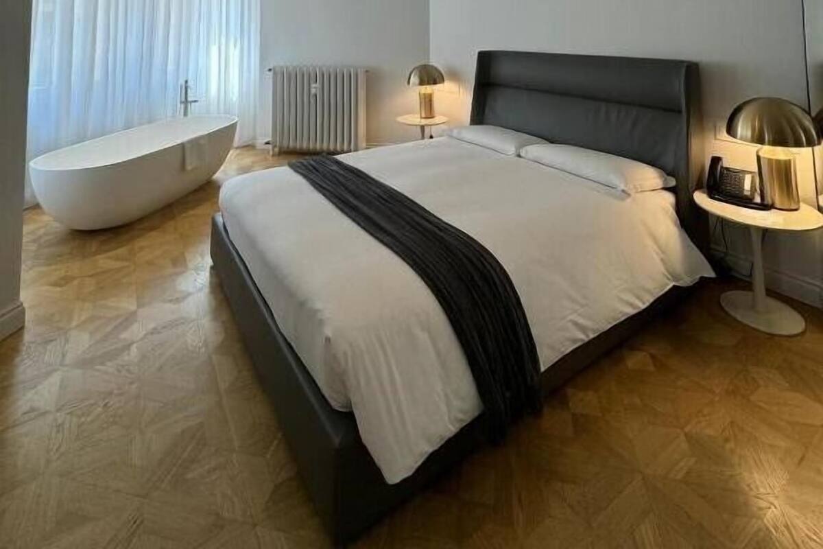 A modern bedroom with a large bed, a built-in bathtub, a ceiling light fixture, and a radiator.