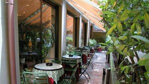 Un patio al aire libre con mesas y sillas, rodeado de plantas y un piso de ladrillo.