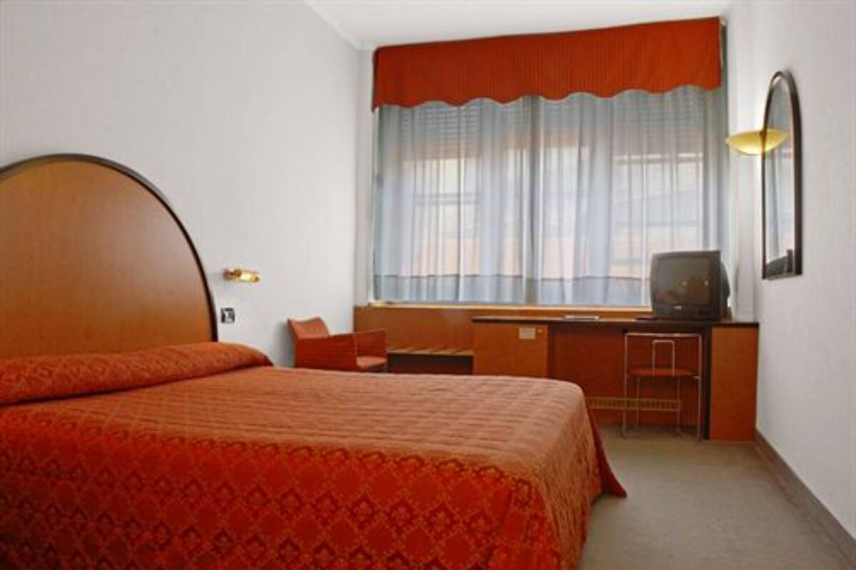 A hotel room with a large bed, a desk with a chair, a television, and a window with curtains.