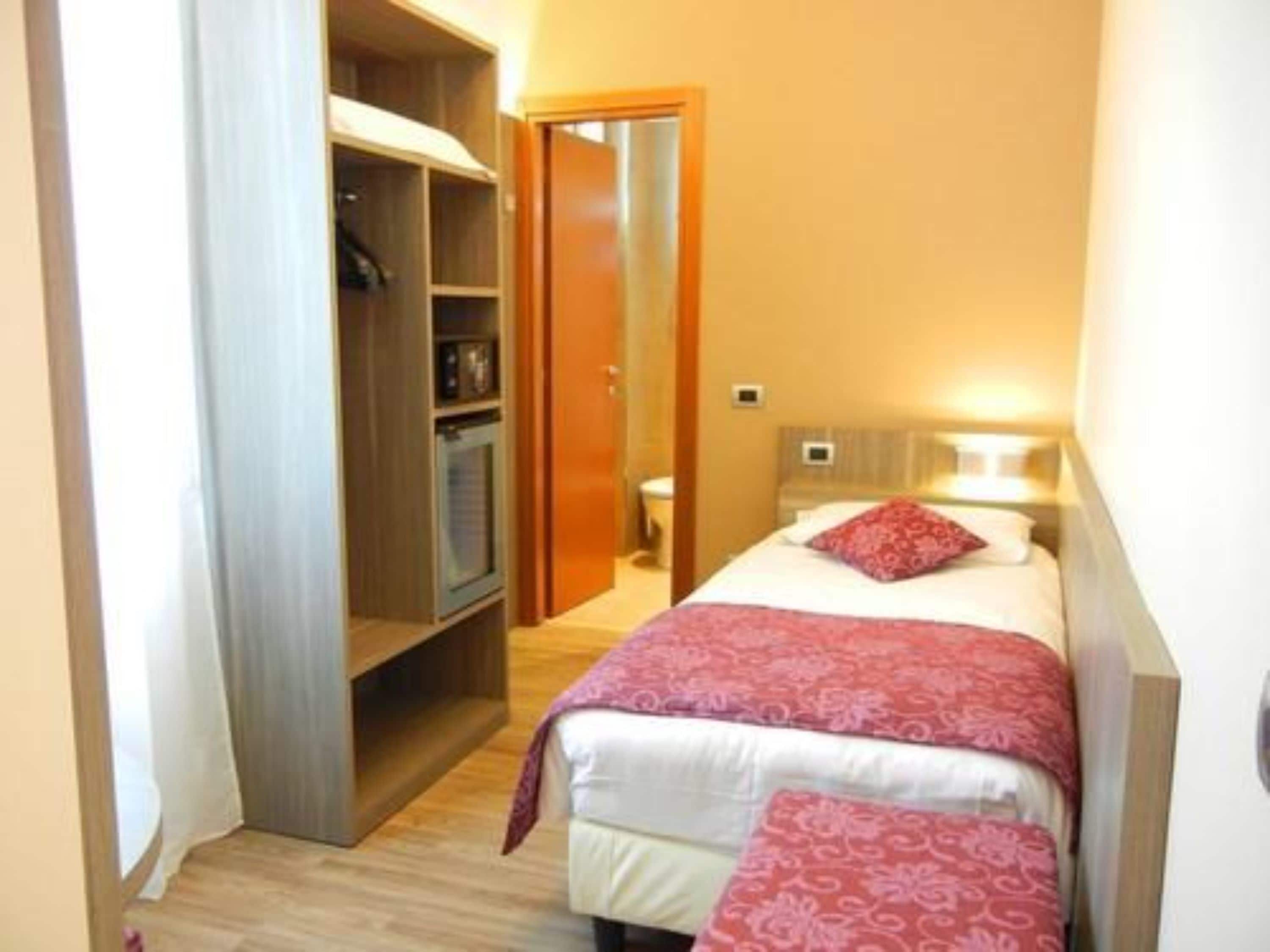 A narrow hallway leading to a bedroom with a bed, a bedside table, and a wardrobe.