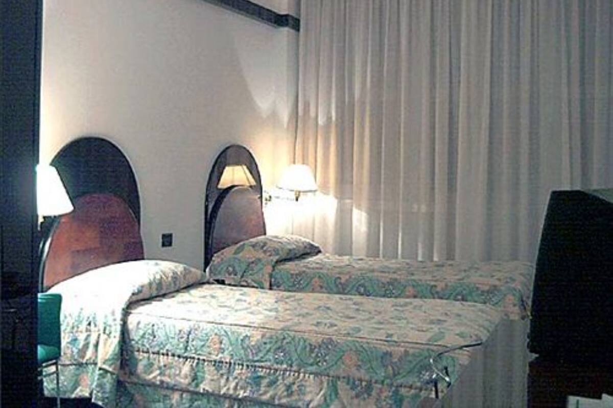 A hotel room with two beds, a wooden headboard, a lamp, and a curtain.