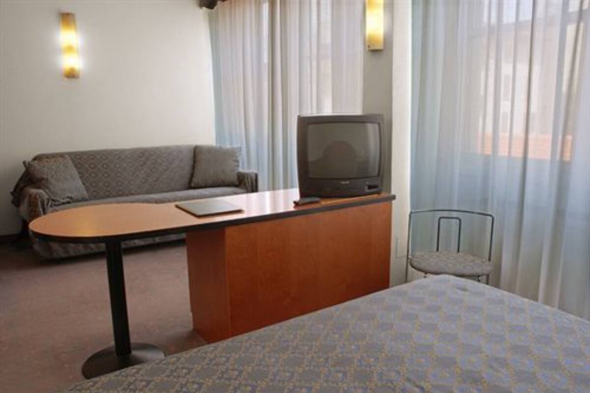 A hotel room with a bed, a desk with a television, a sofa, and a chair.