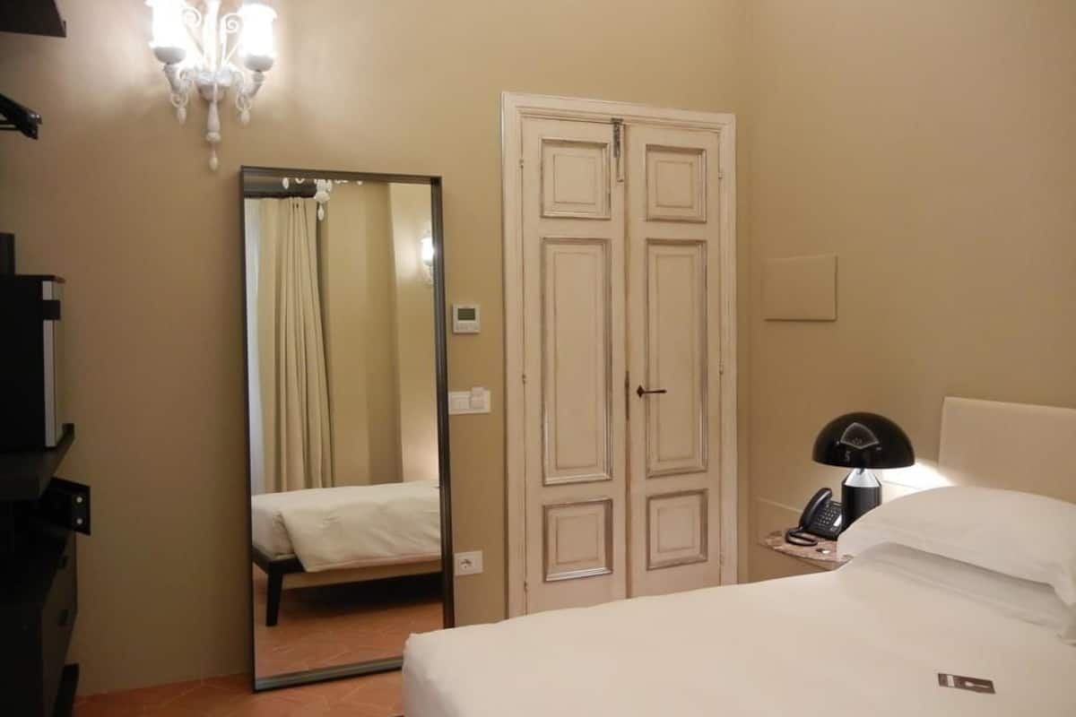 A hotel room with a bed, a mirror, a wardrobe, a desk, and a lamp.