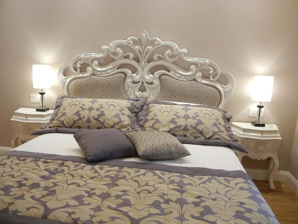 Un lit bien fait, recouvert d’une couvre-lit à motifs et agrémenté d’oreillers, flanqué de deux tables de chevet avec des lampes, le tout placé devant un mur uni.