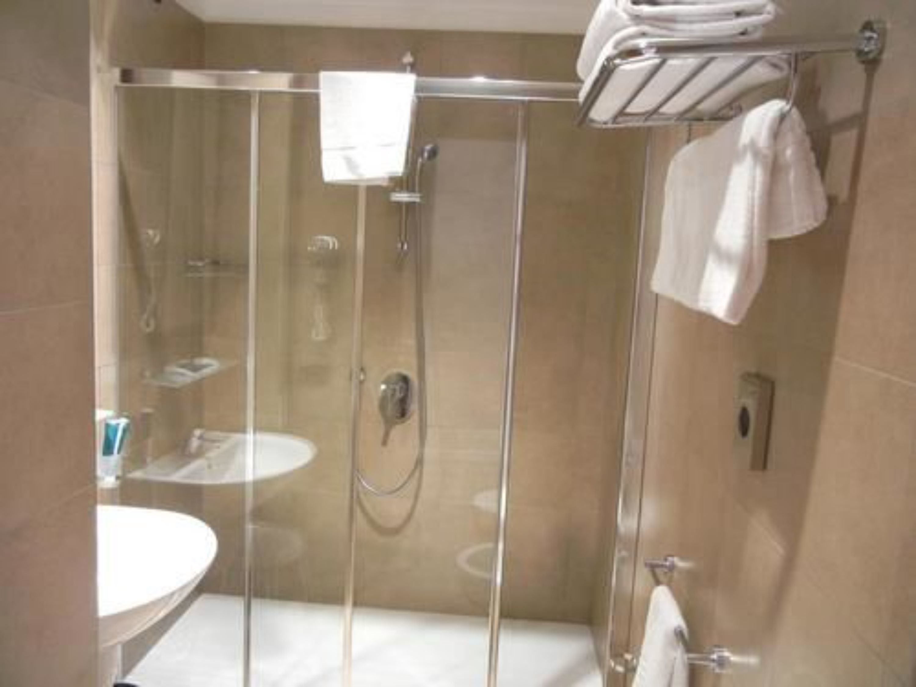 Et brusekabine med glasdøre, en håndklæderadiator over, en vask og et toilet.