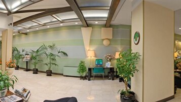 A reception area with a green and beige color scheme, potted plants, a desk with a computer, and a wall-mounted clock.