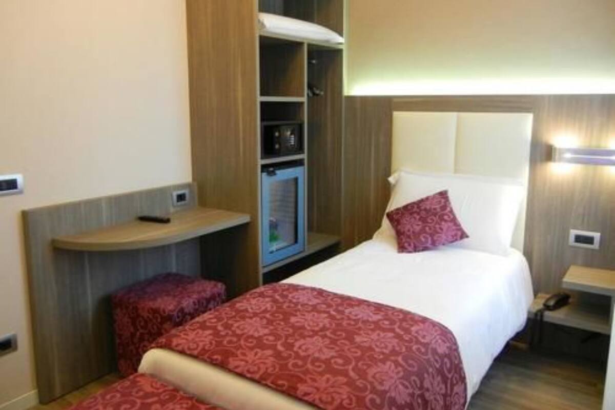 A compact hotel room with a bed, a small desk, a wardrobe, and a built-in microwave.