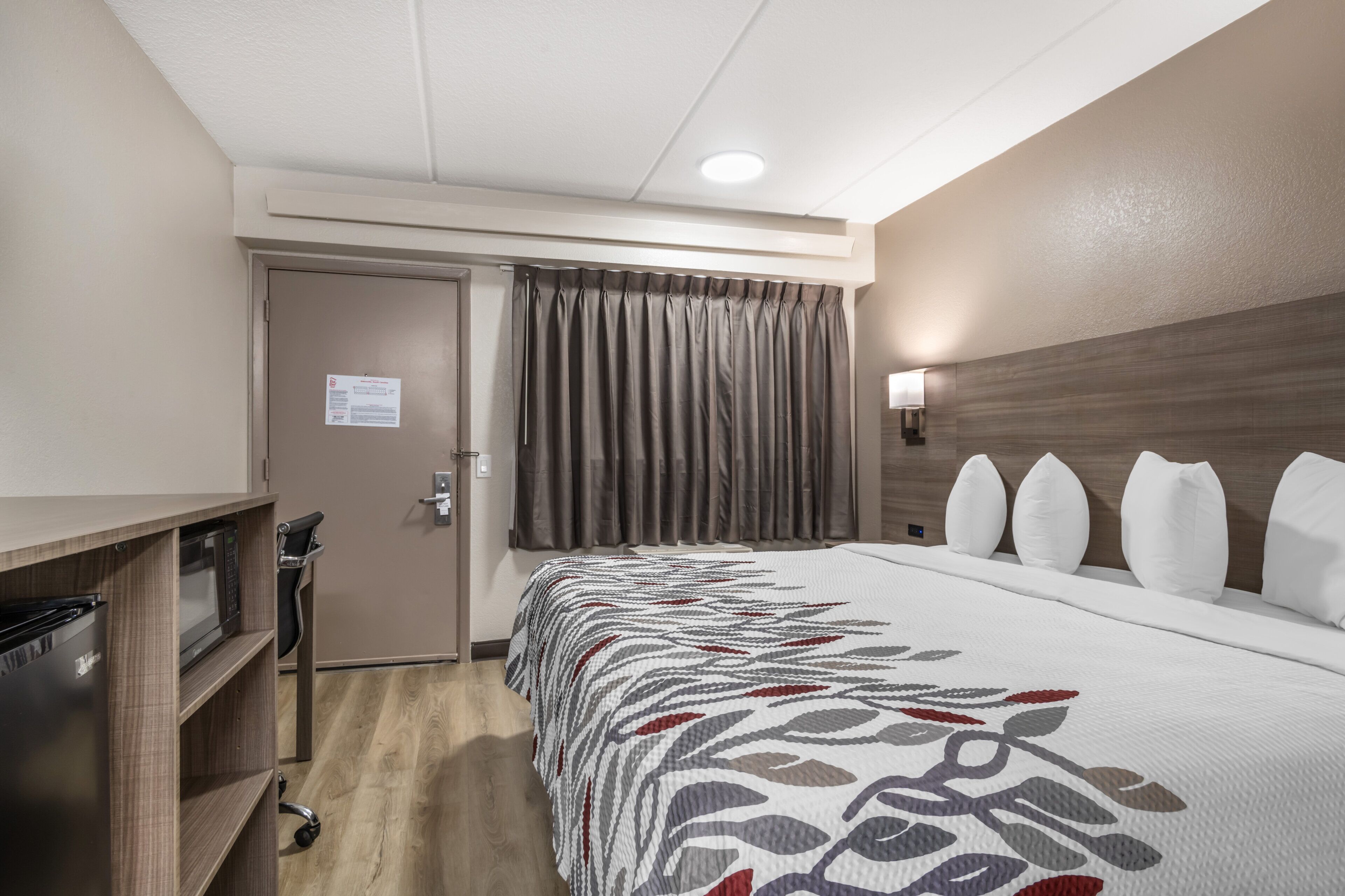 Une chambre d’hôtel avec un lit, un bureau, une chaise, une armoire et une porte.