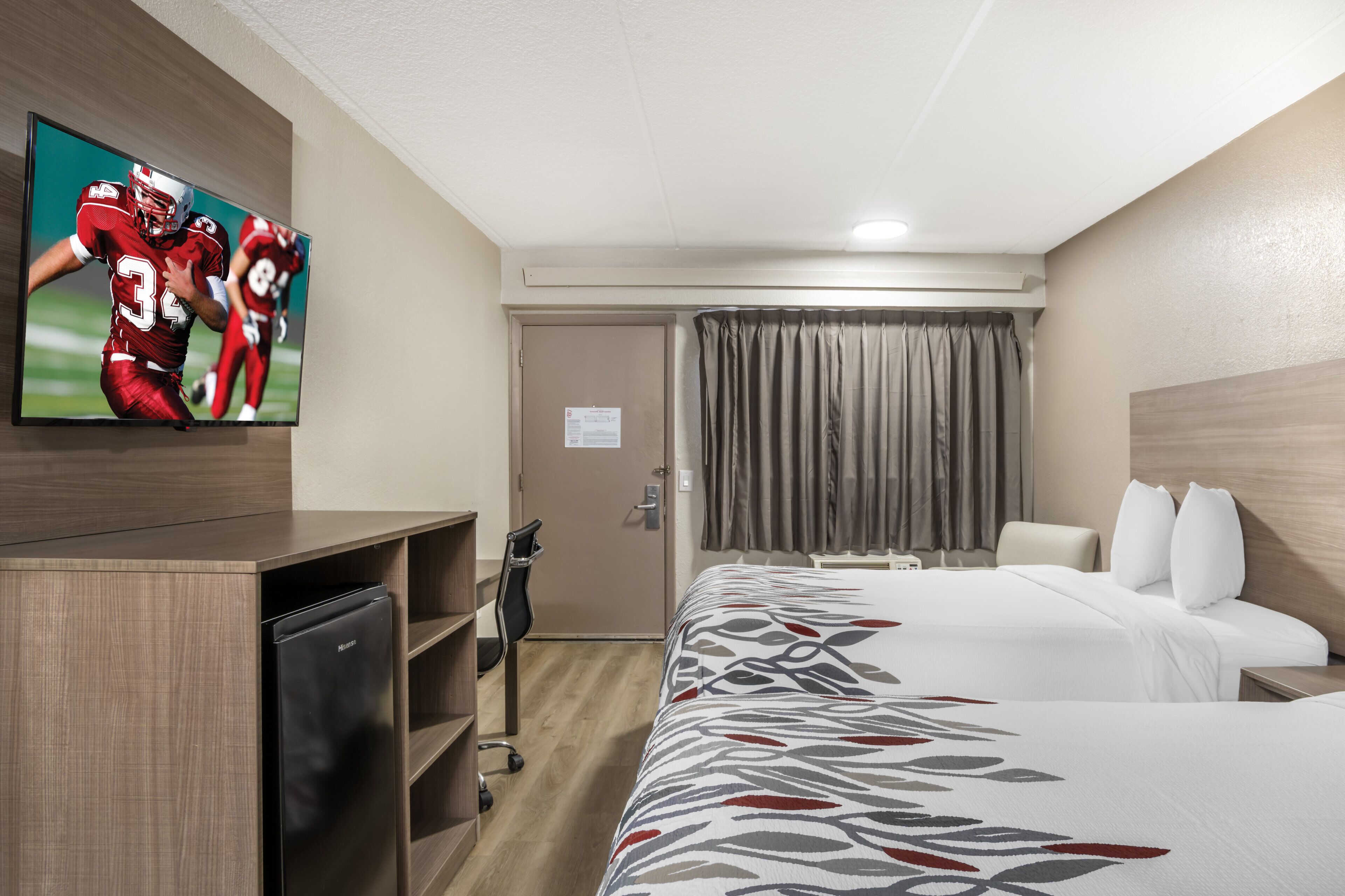 A hotel room with a bed, a desk with a television, a chair, a wardrobe, and a door.