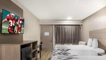 A hotel room with a bed, a desk with a television, a chair, a wardrobe, and a door.