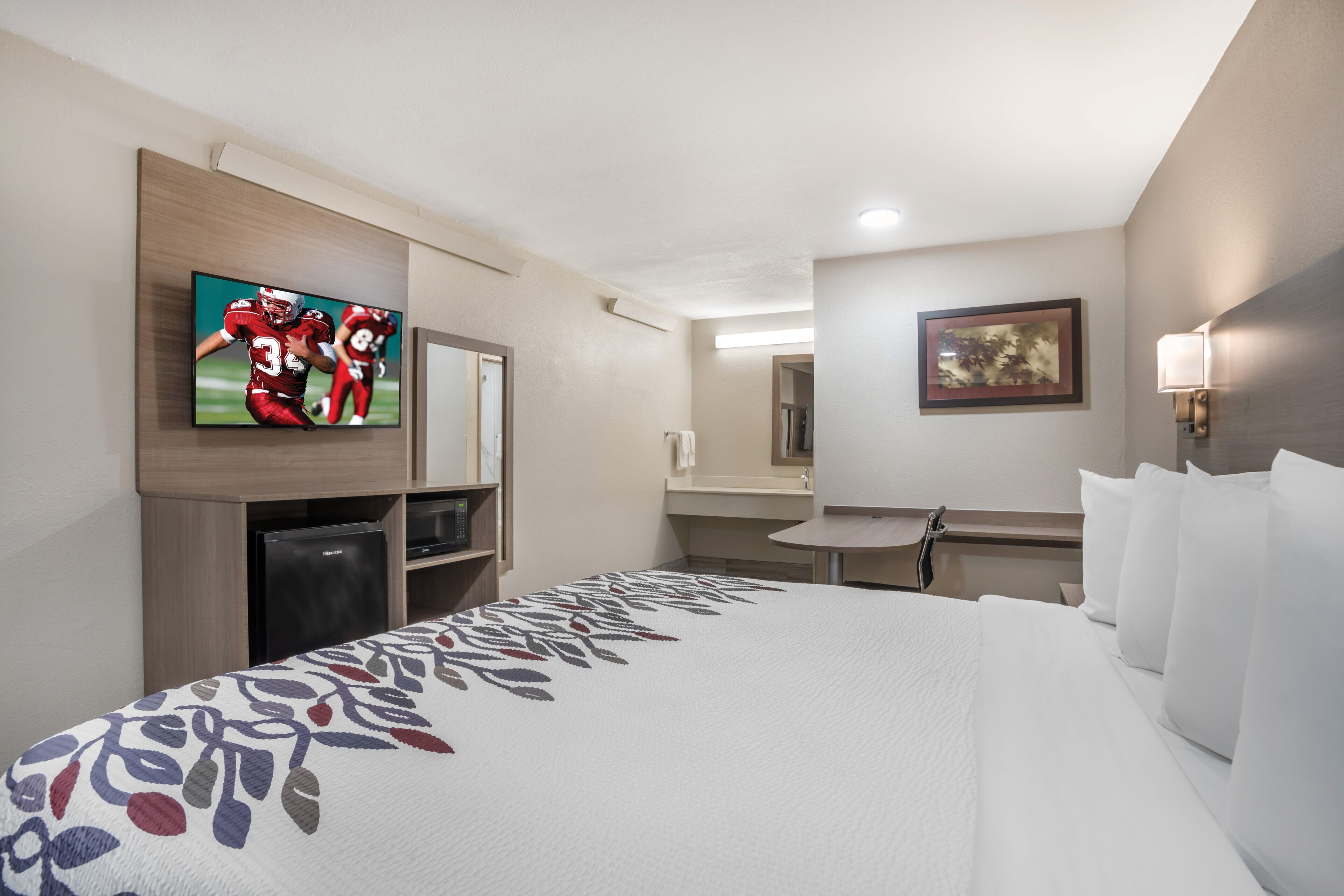 A hotel room with a bed, a television, a desk, and a bathroom.