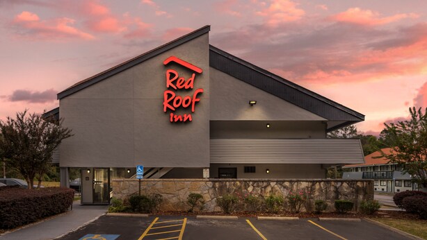A Red Roof Inn with a modern architectural design, featuring a prominent neon sign, a parking lot with handicapped accessibility, and a stone facade. - Red Roof Inn Greenville (Greenville)