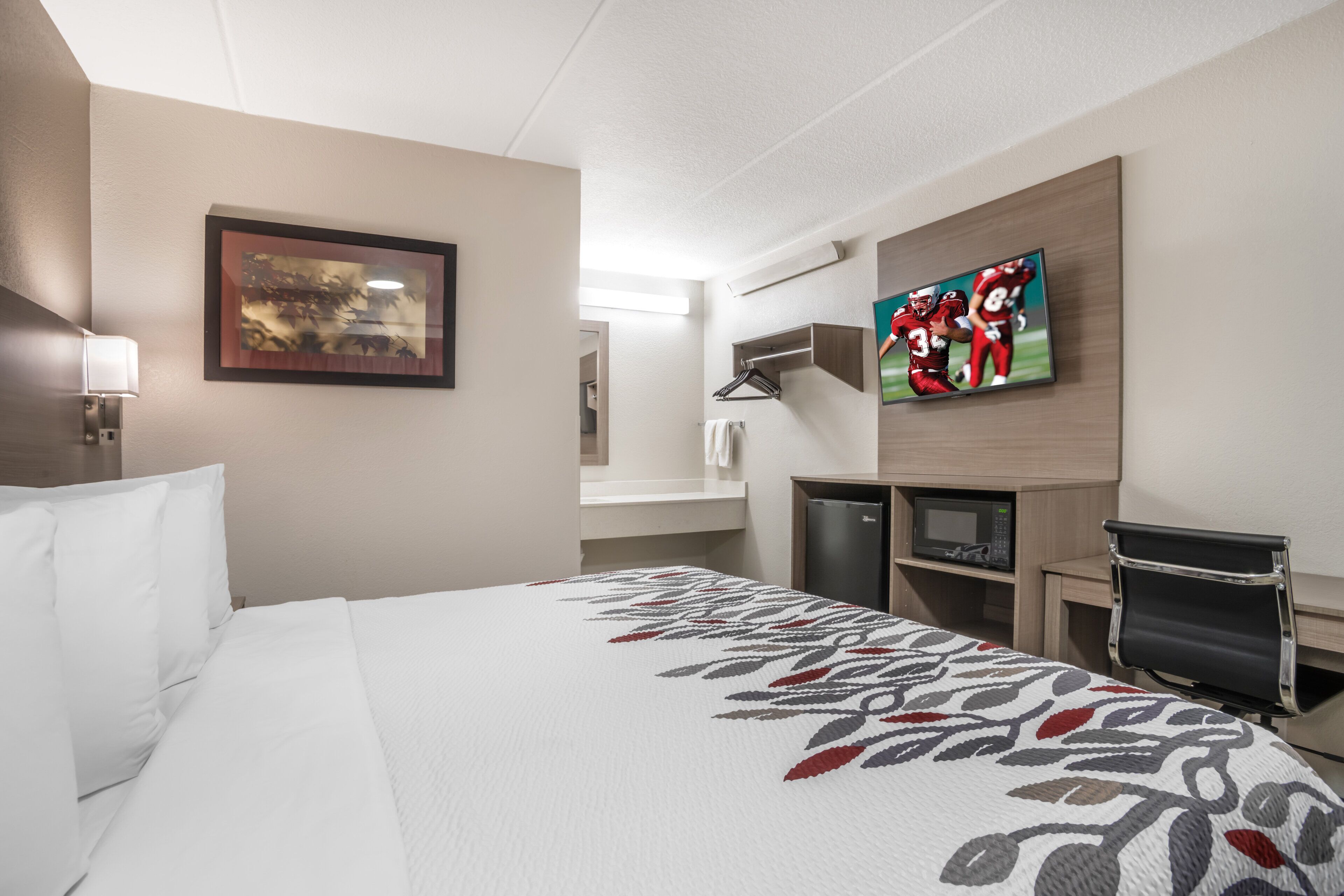 A hotel room with a large bed, a television, a desk with a computer, and a mirror.