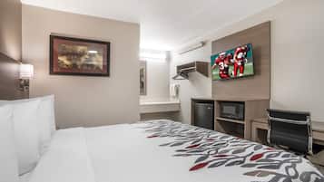 A hotel room with a large bed, a television, a desk with a computer, and a mirror.