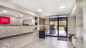 A reception area with a tiled floor, a reception desk, a clock, and a sign offering free Wi-Fi. - Red Roof Inn Greenville (Greenville)