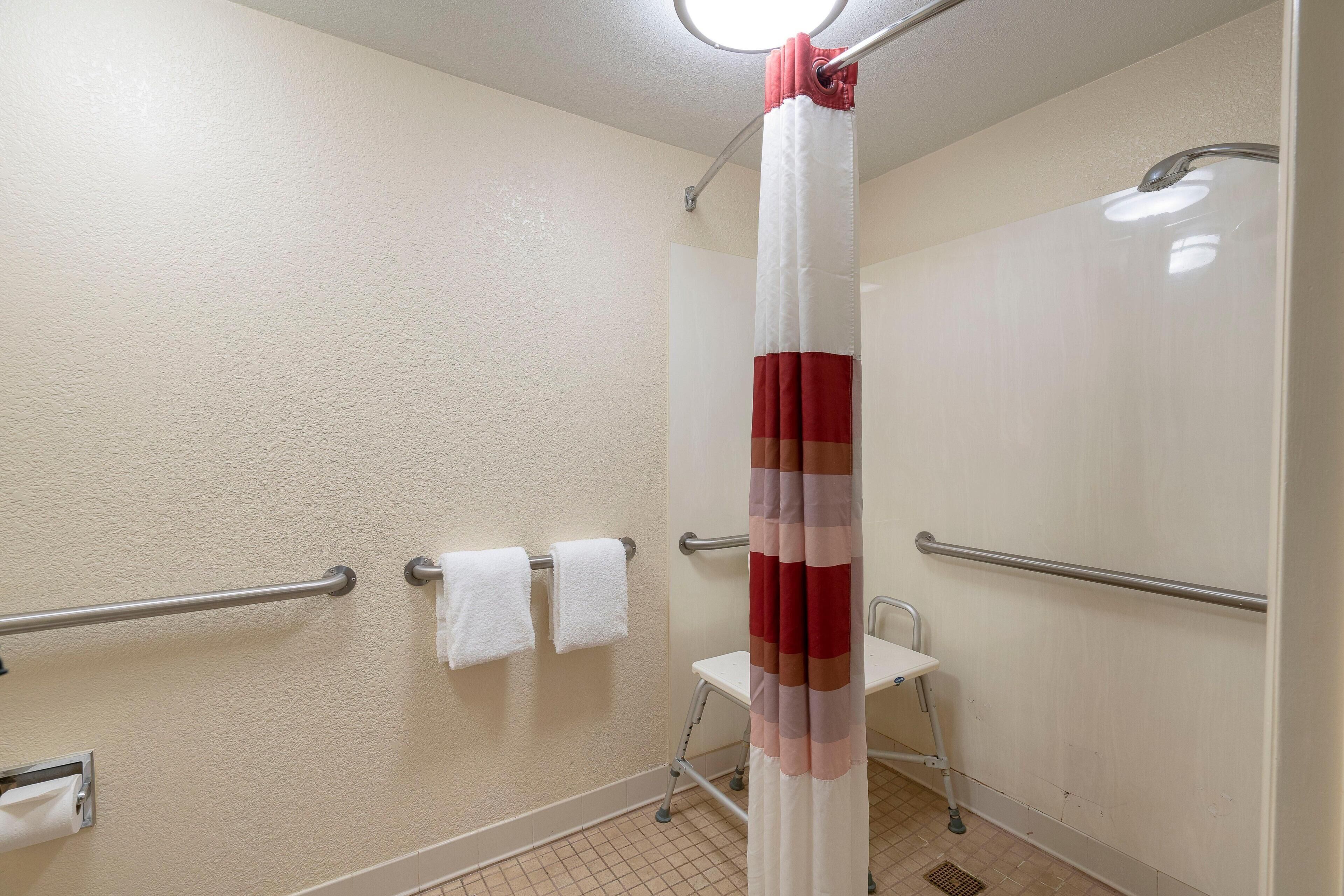 Une salle de bain avec un rideau de douche, des barres d’appui et deux serviettes blanches sur un porte-serviettes.