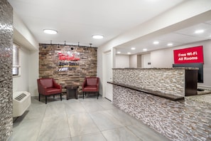A reception area with a stone wall, two red chairs, a small table, and a sign indicating free Wi-Fi in all rooms. - Red Roof Inn Greenville (Greenville)
