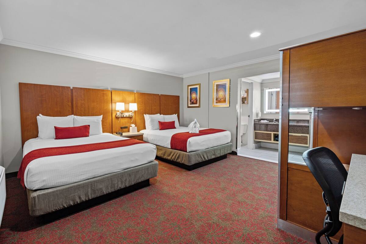 A hotel room with two beds, a desk, and a bathroom visible through an open door.
