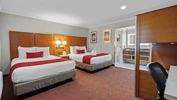 Une chambre d’hôtel avec deux lits, un bureau et une salle de bain visible à travers une porte ouverte.