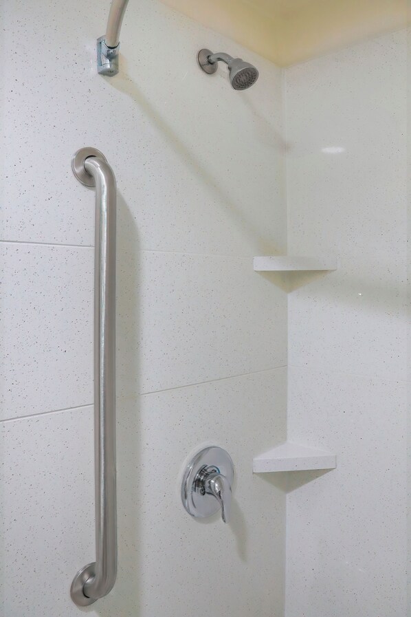 A shower area with a grab bar, a handheld showerhead, and a wall-mounted faucet.