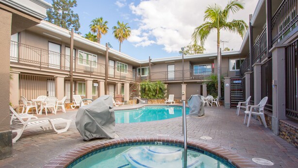 A pool area with lounge chairs and a hot tub, surrounded by a building with balconies and palm trees.