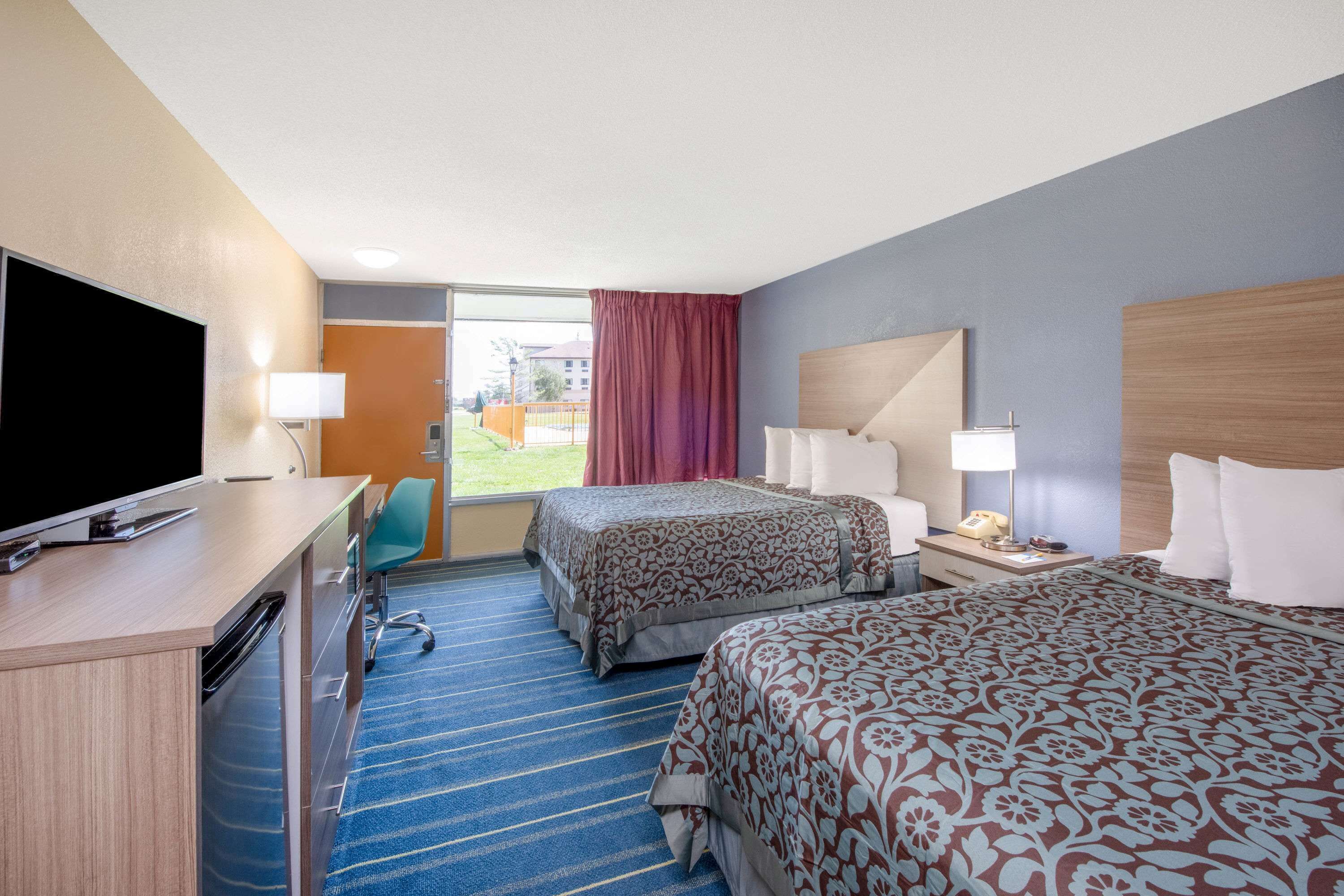 A hotel room with two beds, a desk with a TV, a chair, and a window with a view of the outside.