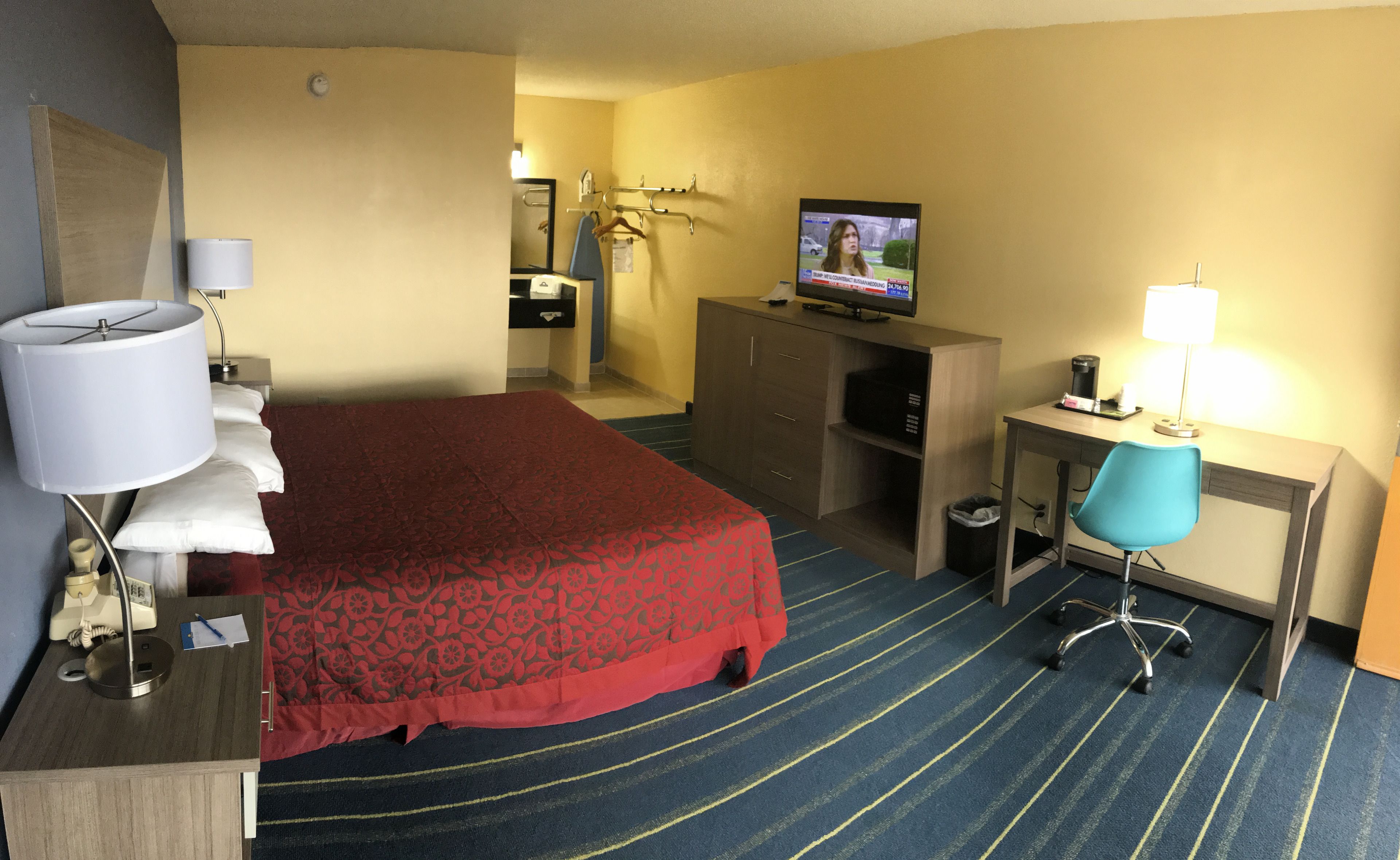 Habitación de hotel con cama, escritorio, silla, televisión y una mesita de noche con lámpara.