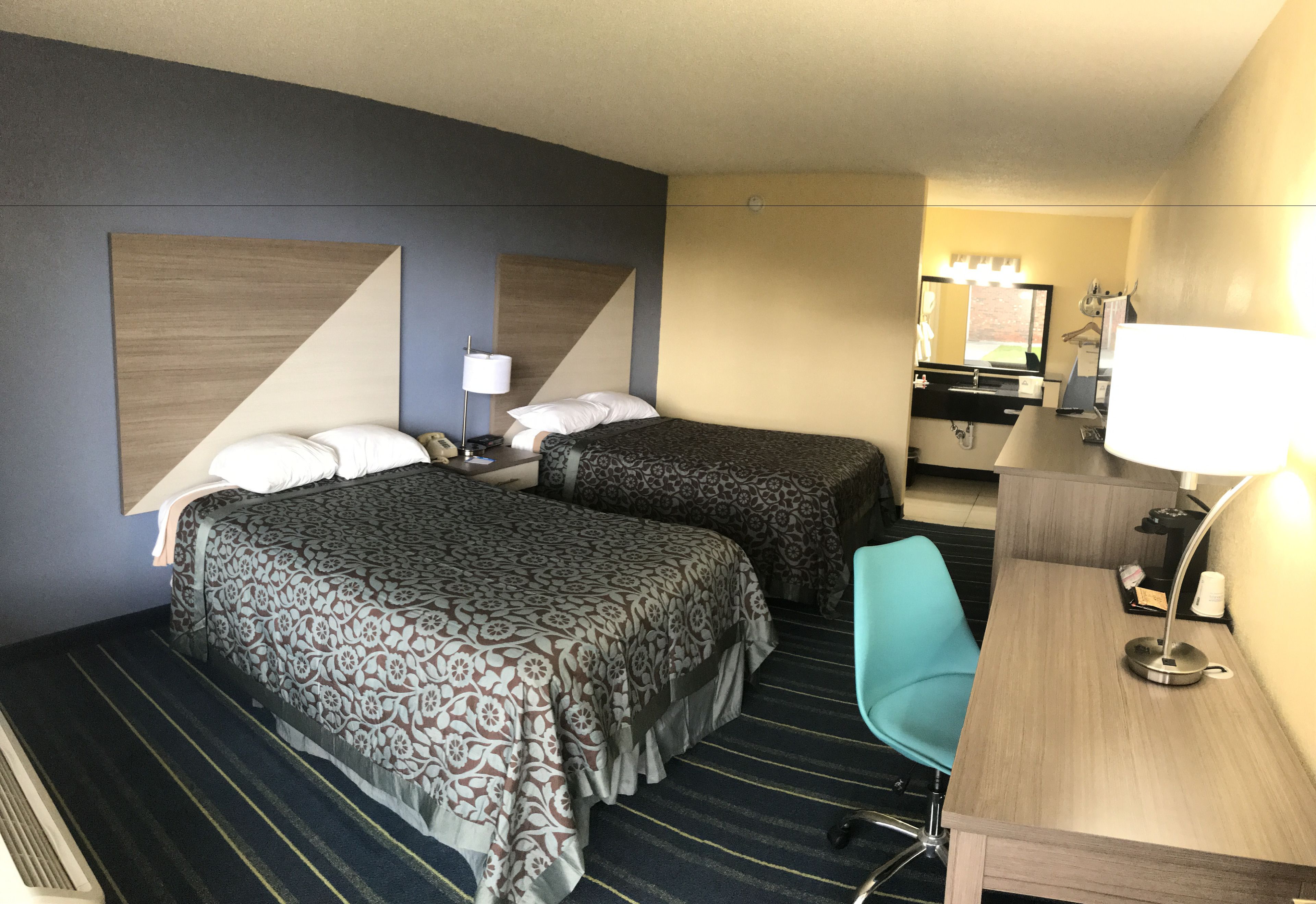 A hotel room with two beds, a desk, a chair, a mirror, and a lamp.