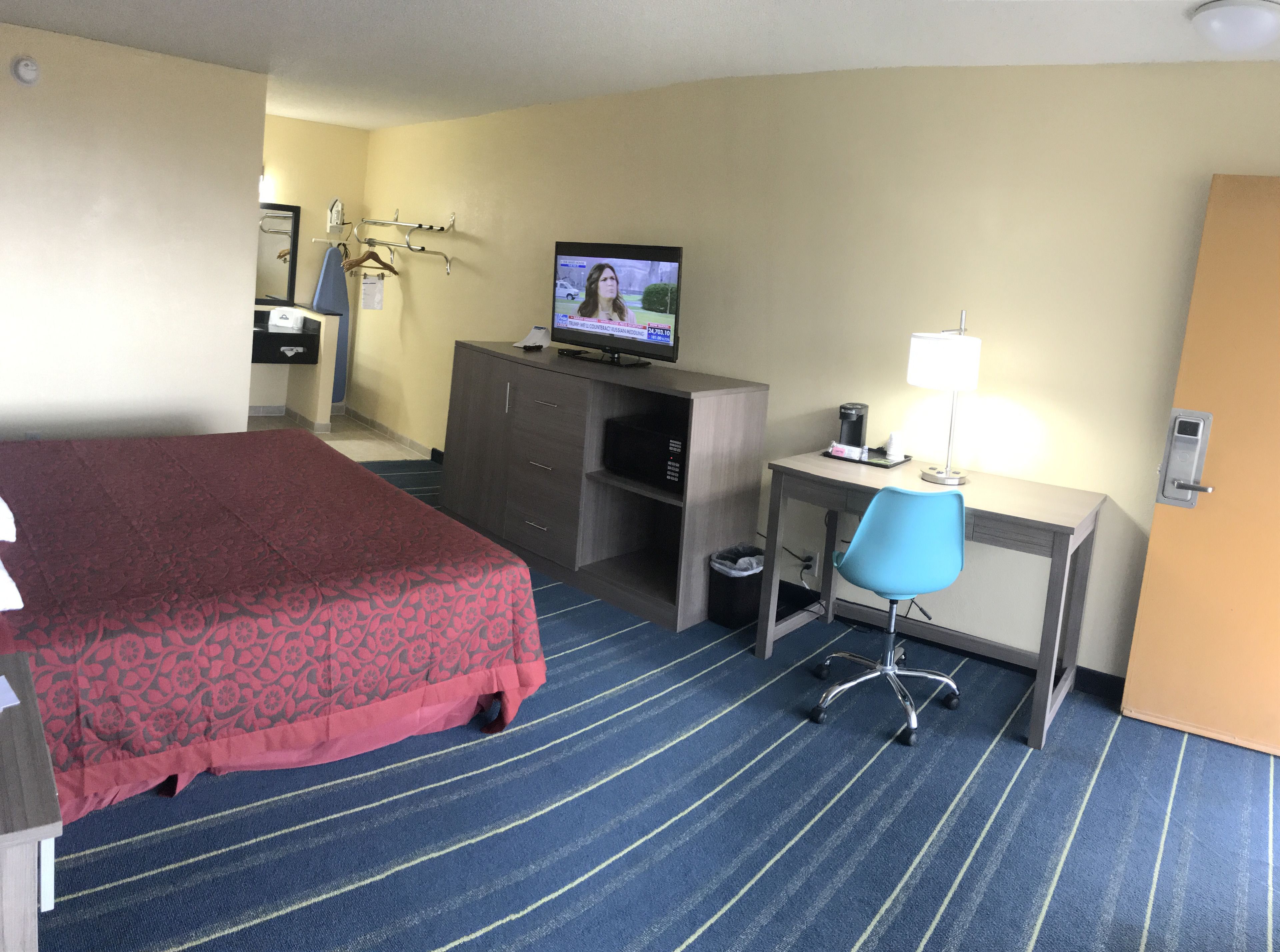 A hotel room with a bed, a desk, a chair, a television, and a trash bin.