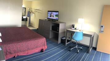 A hotel room with a bed, a desk, a chair, a television, and a trash bin.