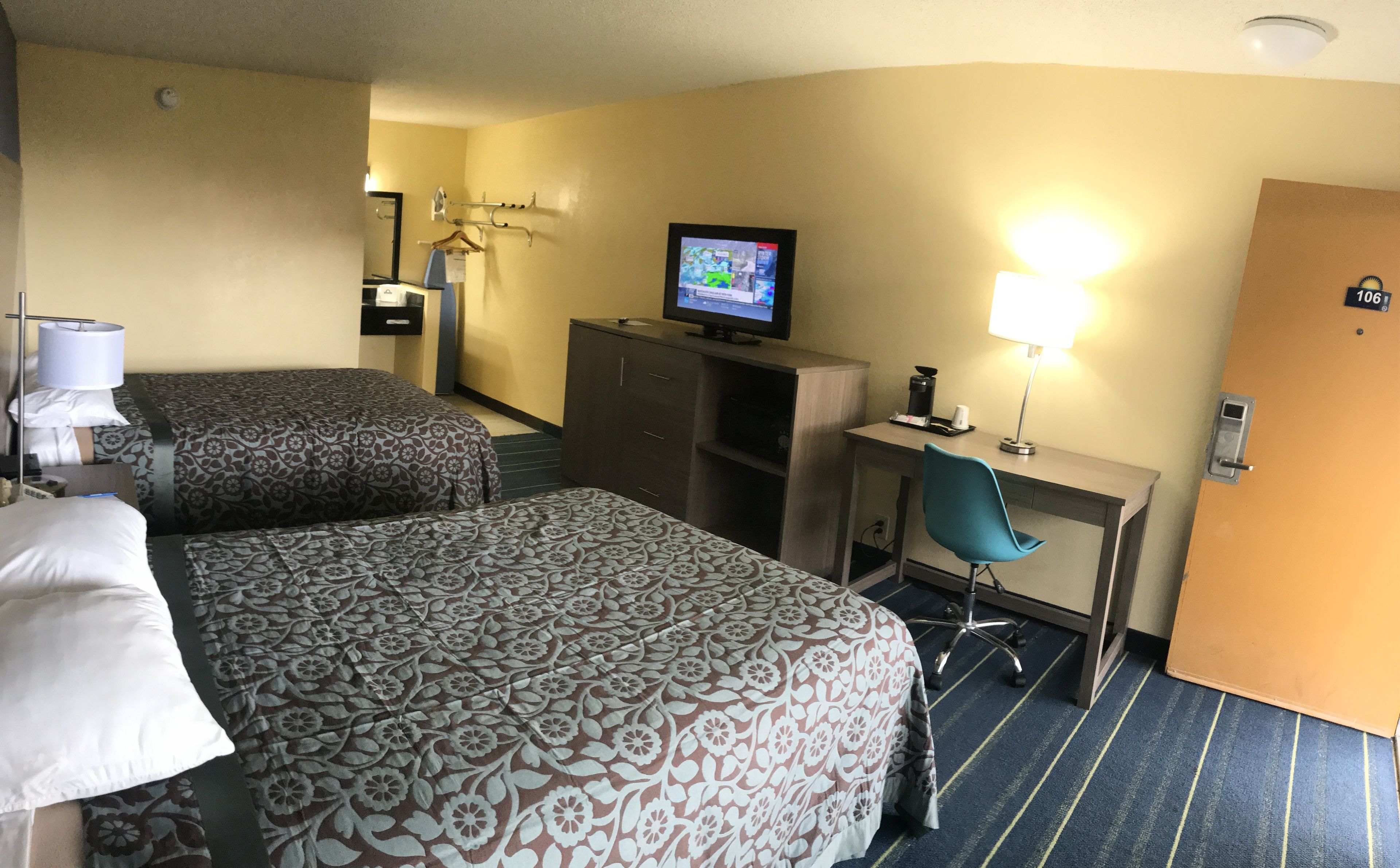 Een hotelkamer met twee bedden, een bureau, een stoel, een televisie en een lamp.