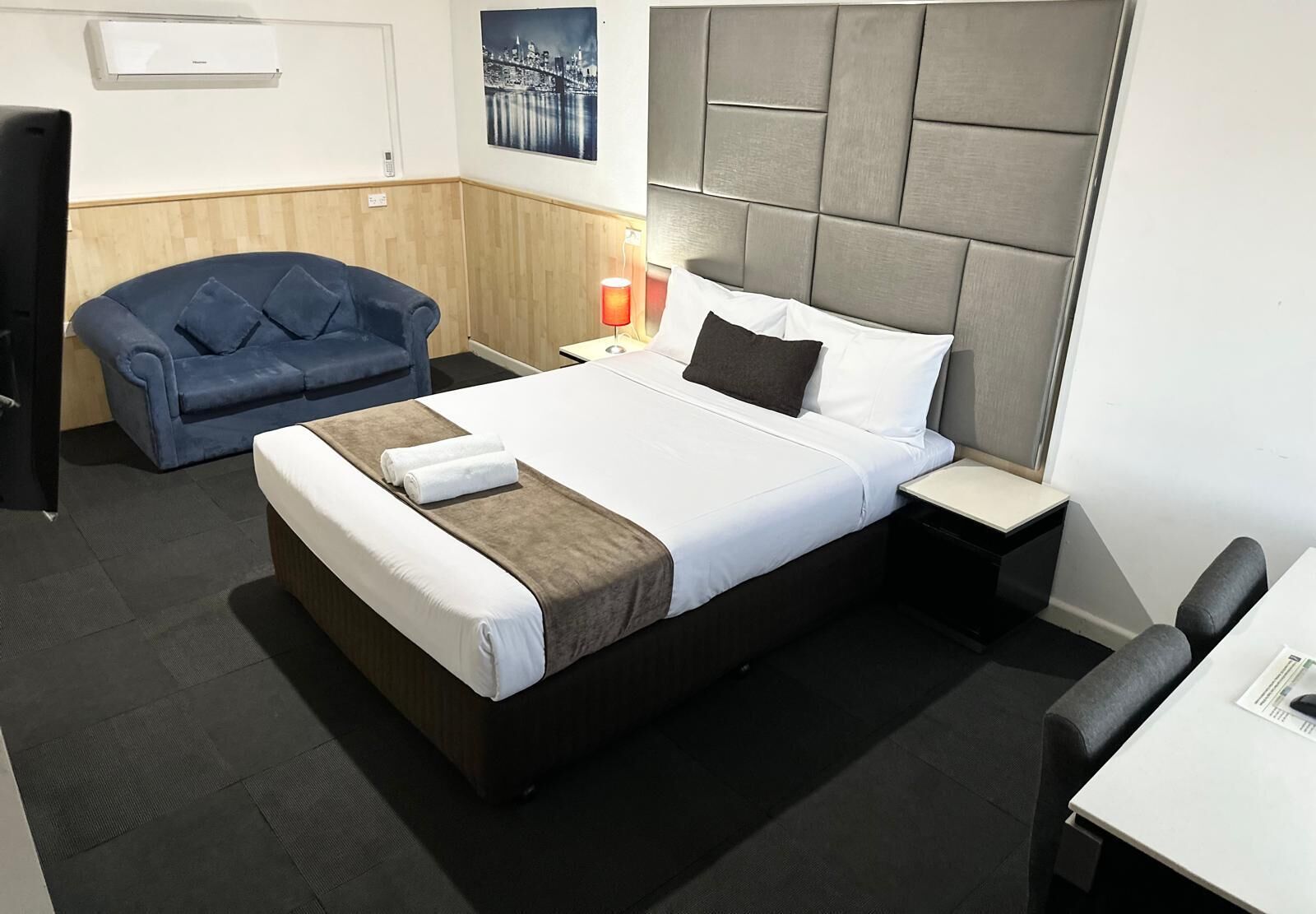 Una habitación de hotel con una cama grande, un sofá azul, un escritorio y una mesita de noche con lámpara.