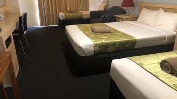 Ein Hotelzimmer mit zwei Betten, einem Schreibtisch, einem Stuhl, einem Nachttisch mit Lampe und einem Fenster mit Vorhängen.