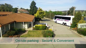 A building with a covered parking area, a parked car, and a bus.