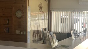 A reception desk with a clock, informational posters, and a window with blinds.