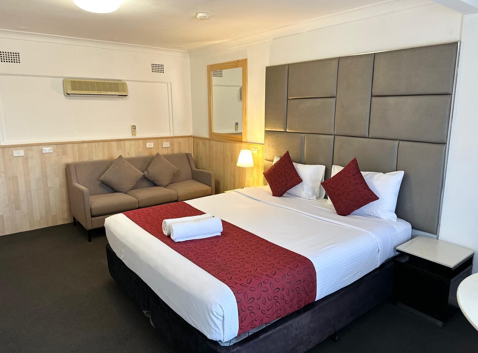 Hotellihuone, jossa on sänky, sohva, yöpöytä ja peili.